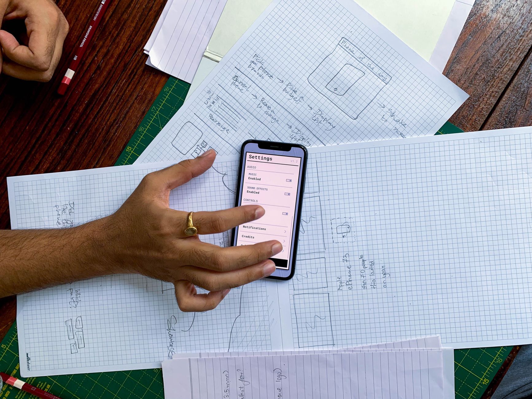 A phone showing an app settings screen on top of hand-drawn app designs