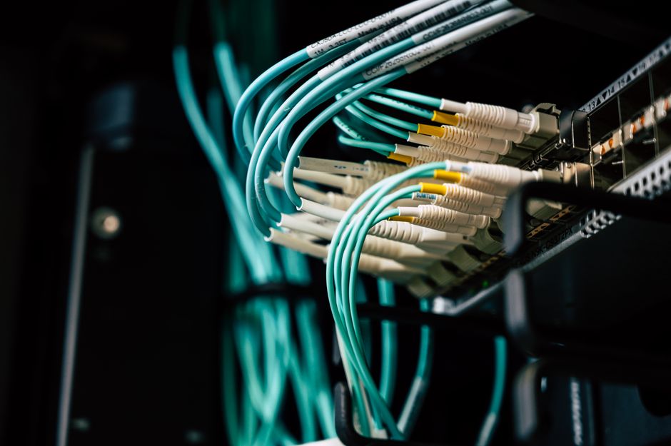 Teal fibre optic cables plugged into a patch panel in a server rack