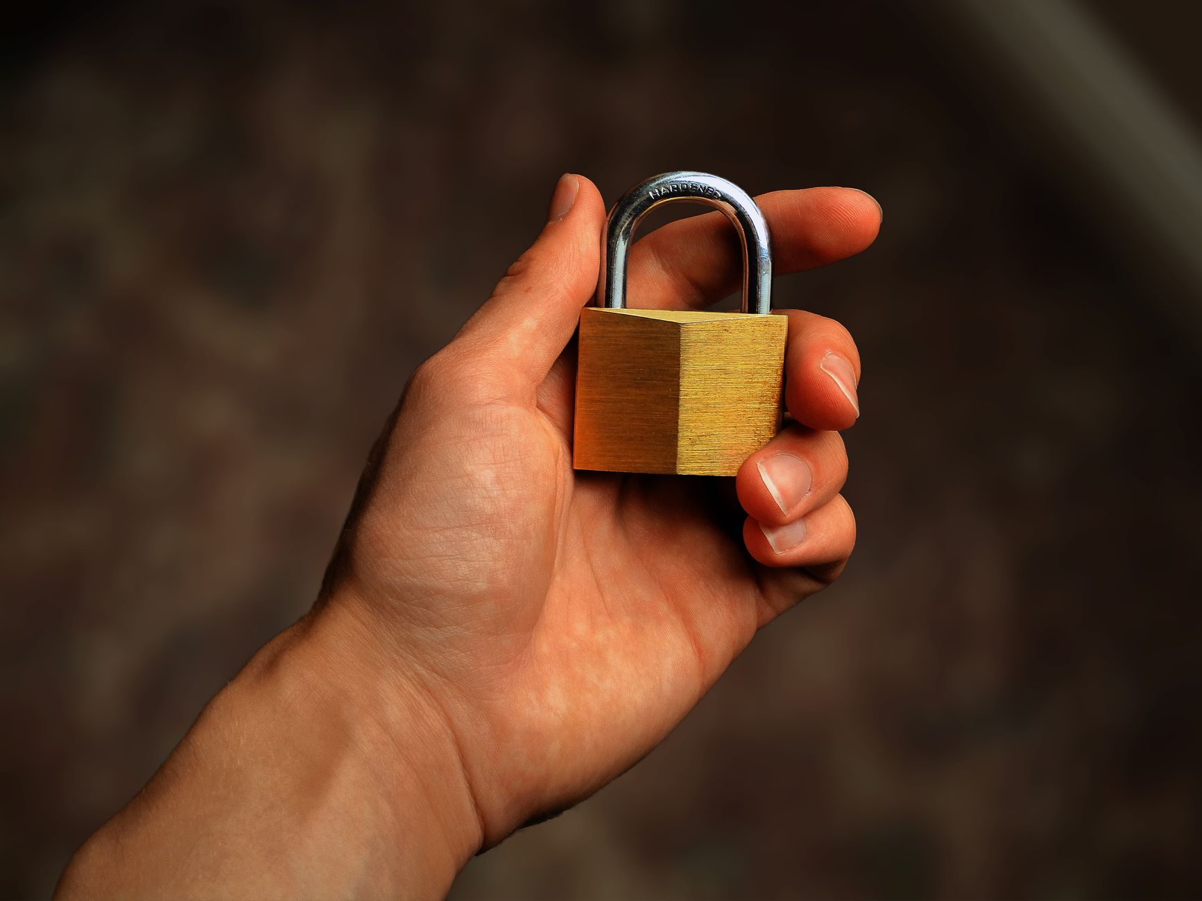 A hand holding a small brass padlock