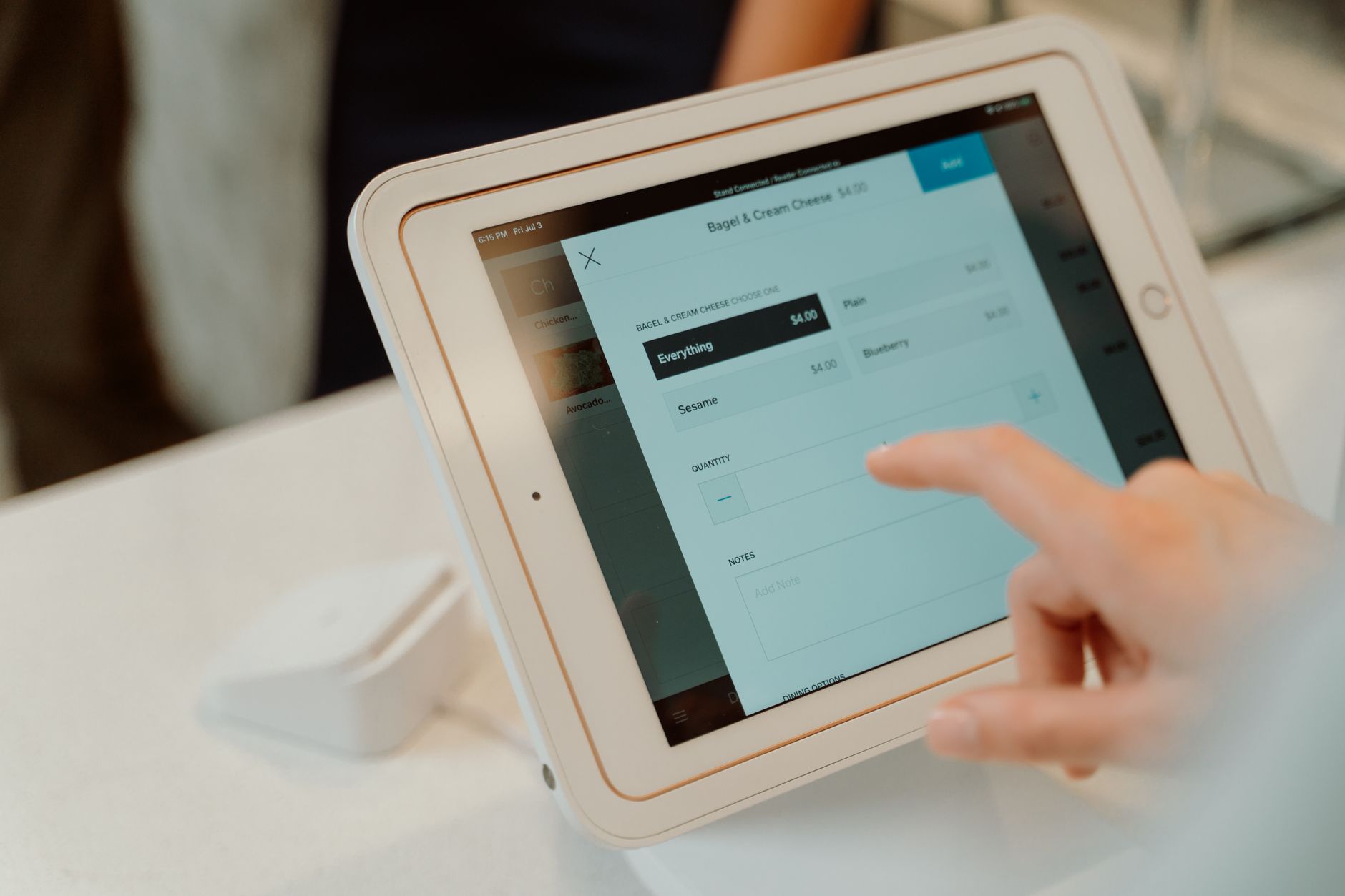 A customer tapping an order on a tablet kiosk with a card reader beside it