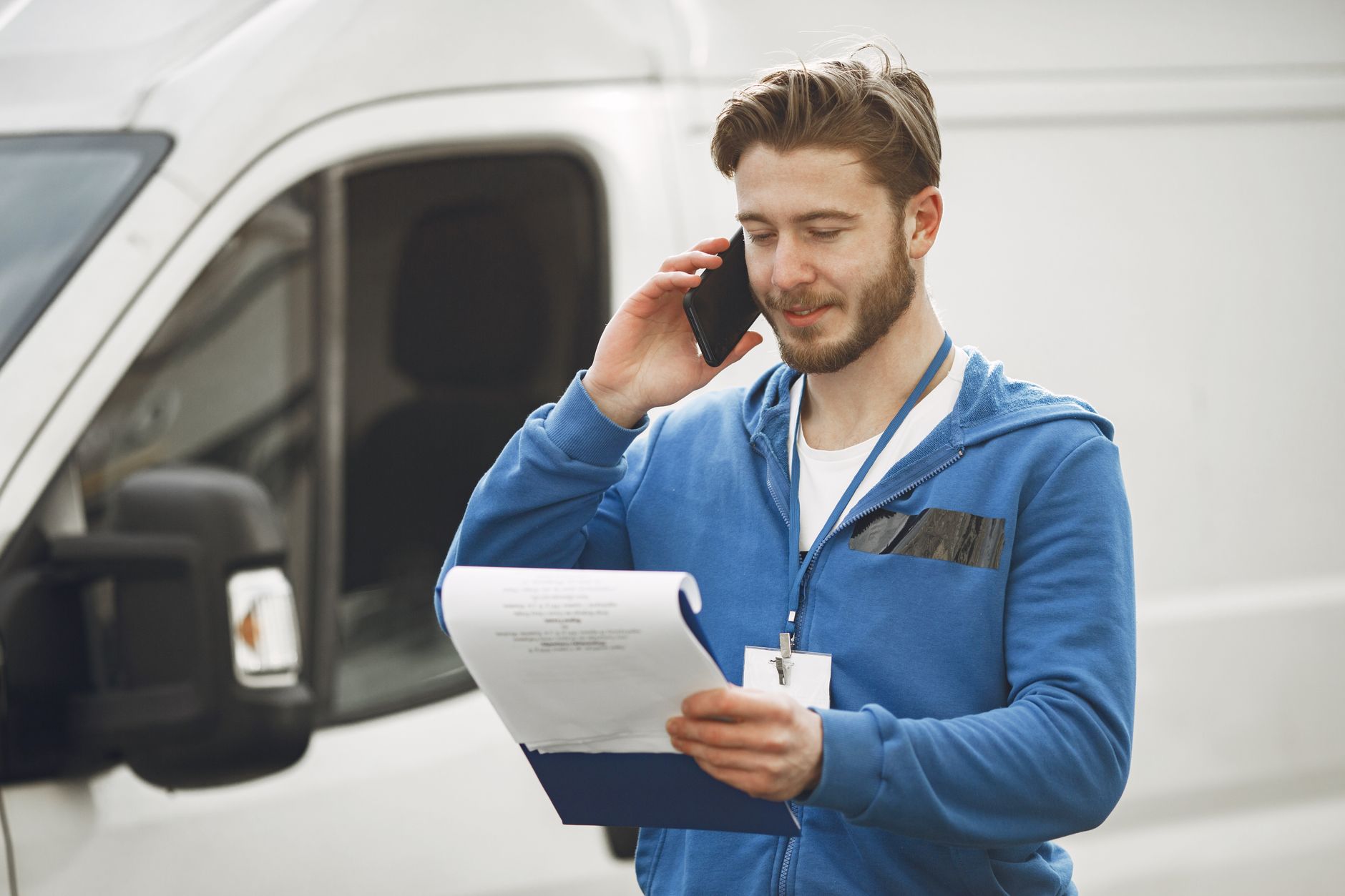 A tradesman on a phone call beside his van, holding a clipboard
